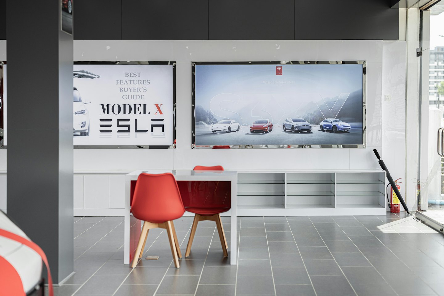 Nowoczesny salon samochodów elektrycznych z czerwonymi krzesłami i plakatami promocyjnymi.