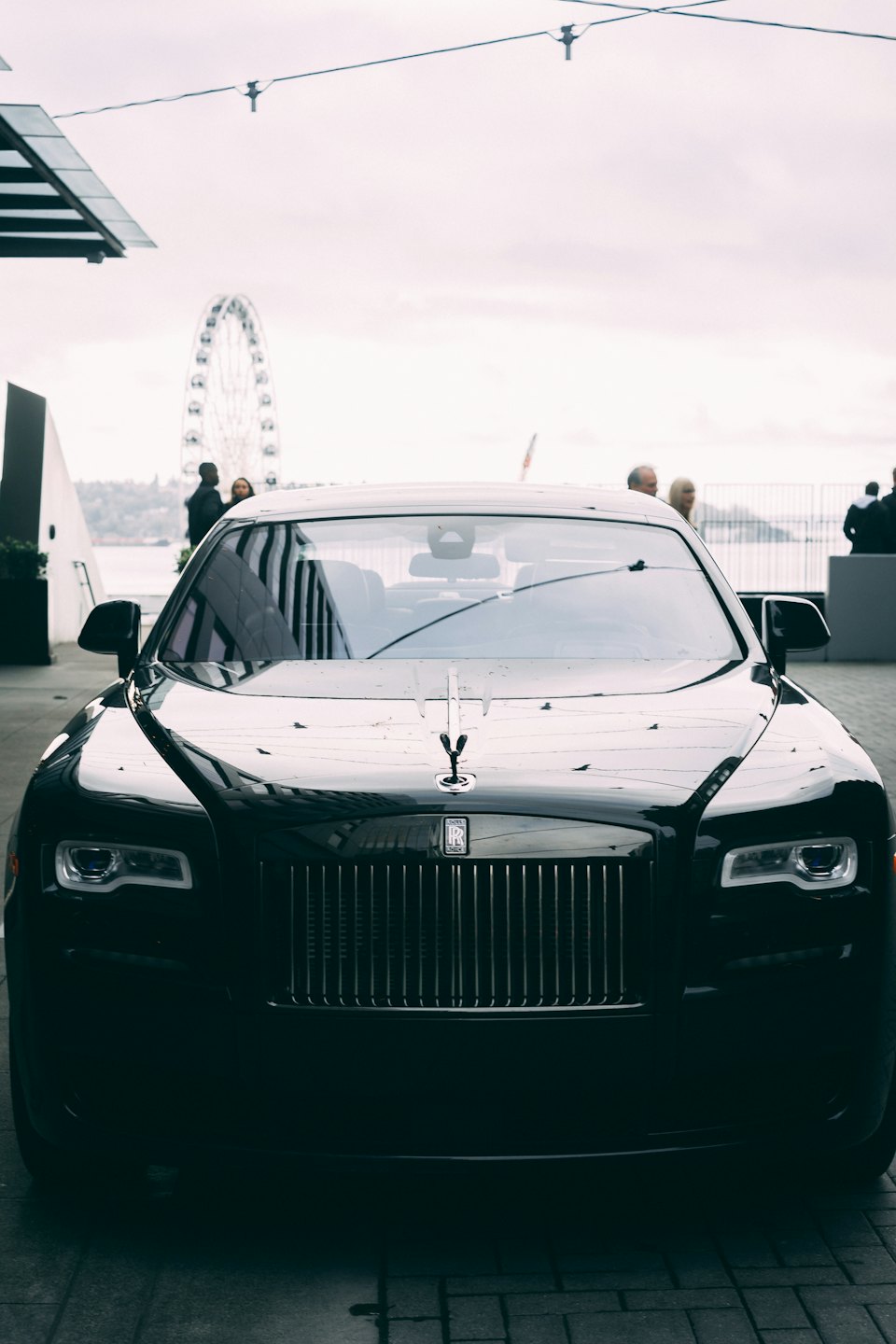Czarny Rolls-Royce zaparkowany przy diabelskim młynie i wodzie.