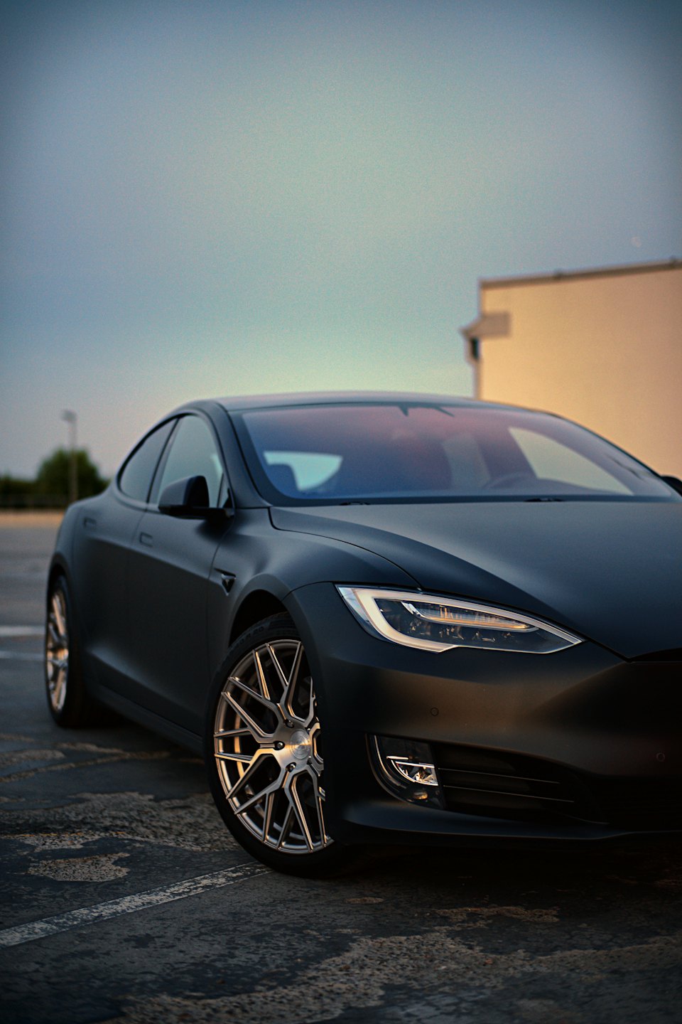 Matowa czarna tesla zaparkowana na betonowym placu o zachodzie słońca.