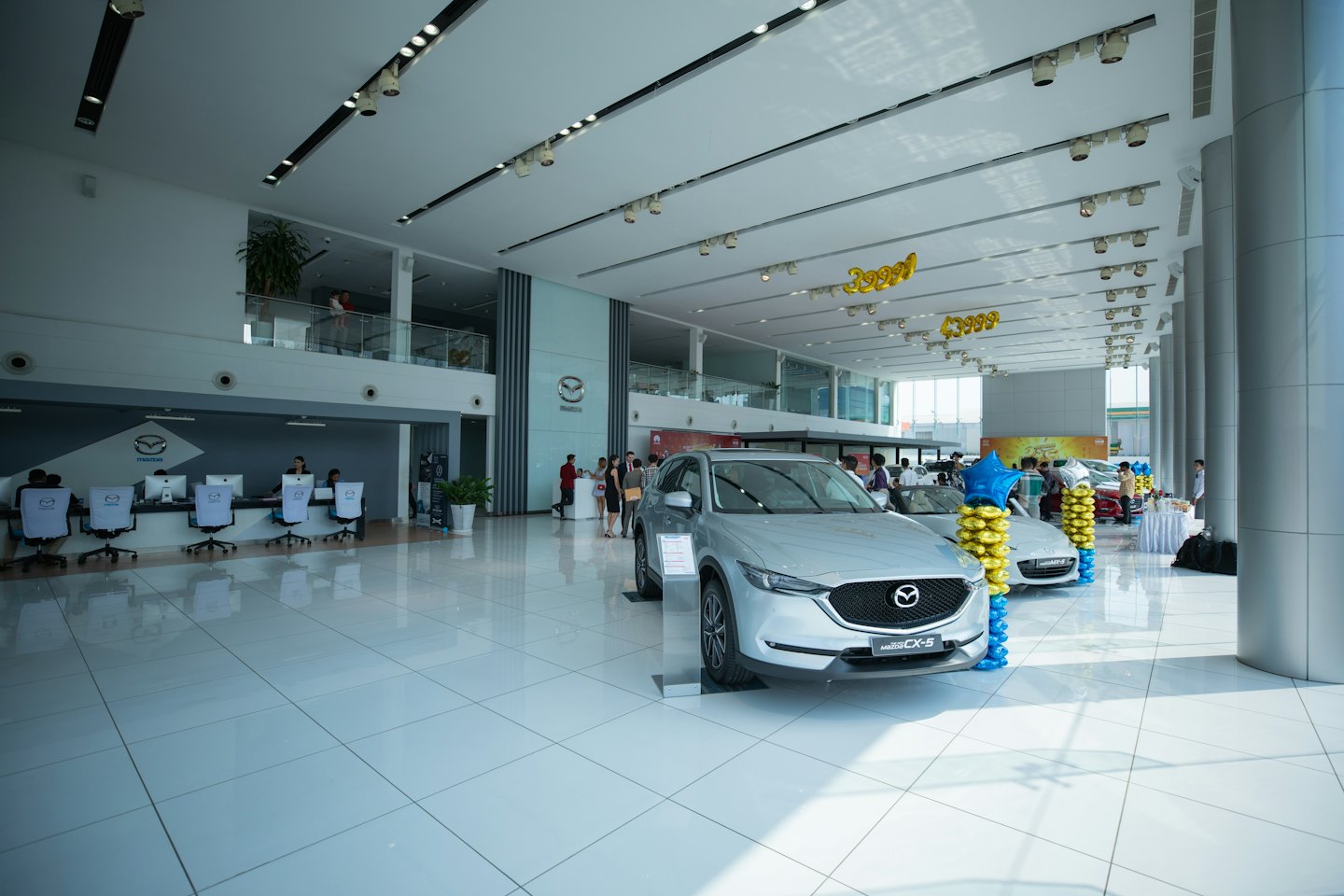 Nowe srebrne samochody marki Mazda wystawione w jasnym salonie dealerskim.
