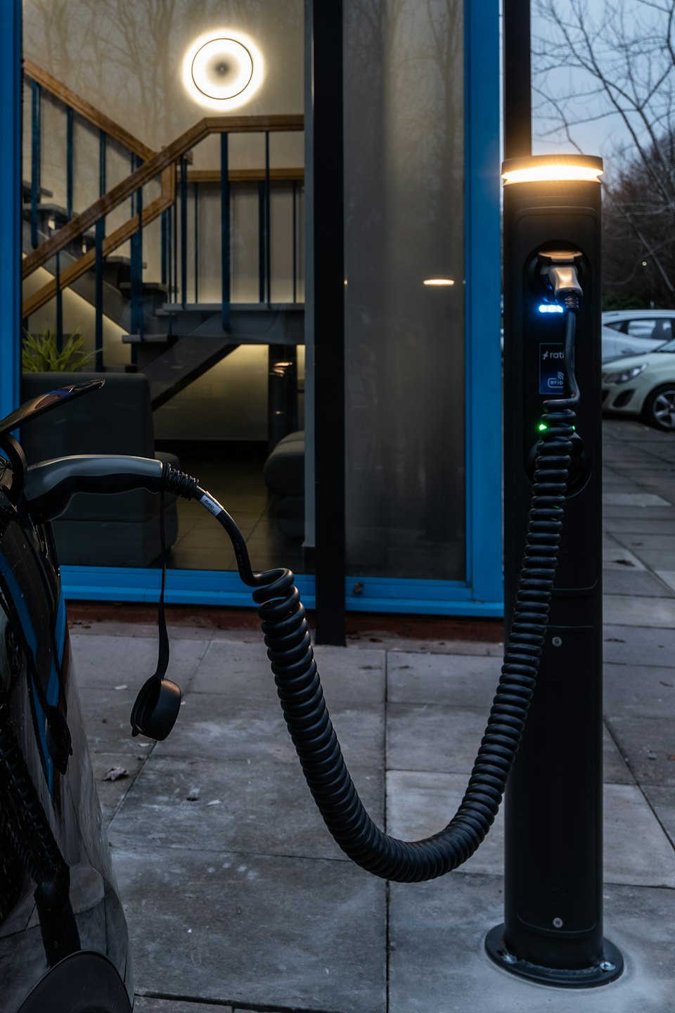 Samochód elektryczny ładuje się na stacji przed nowoczesnym budynkiem.